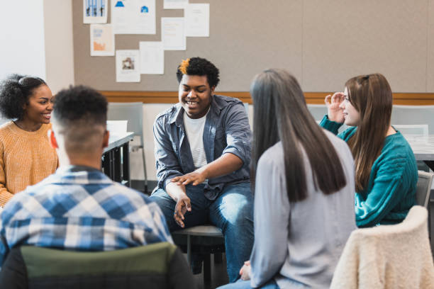 Teenage boy discusses something during support group During a group therapy session, a teenage boy gestures as he talks about something with the people in the group. An attentive female therapist facilitates the meeting. teenager adolescence campus group of people stock pictures, royalty-free photos & images