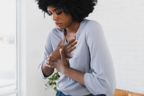 Mid adult woman holds chest Mid adult woman stands up and holds her chest in agony and despair. chest pain stock pictures, royalty-free photos & images