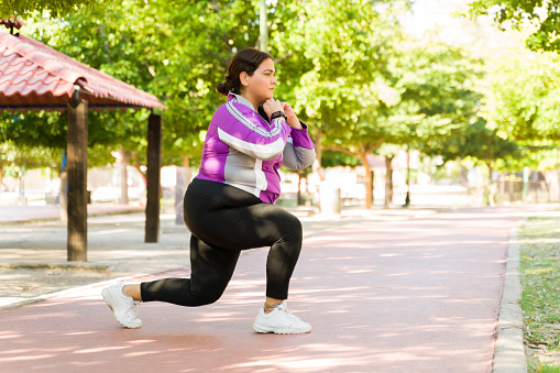 Curvy young woman doing lunges during her workout outdoors. Plus size woman burning calories to lose body fat and weight
