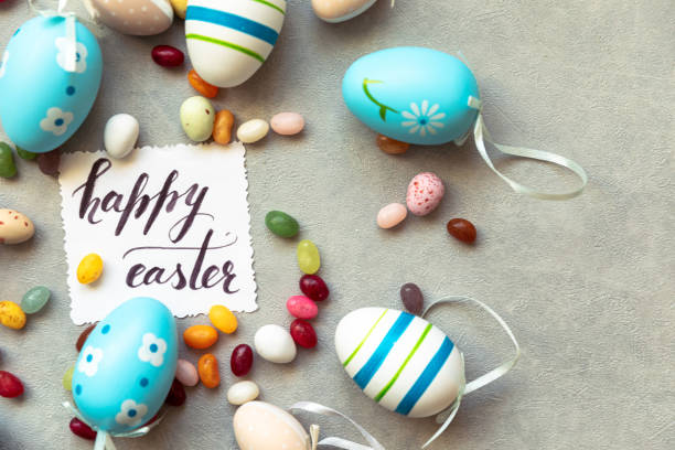 Happy Easter concept. Preparation for holiday. Easter eggs Inscription HAPPY EASTER letters candy chocolate eggs and jellybean sweets on concrete stone grey background. Flat lay top view copy space