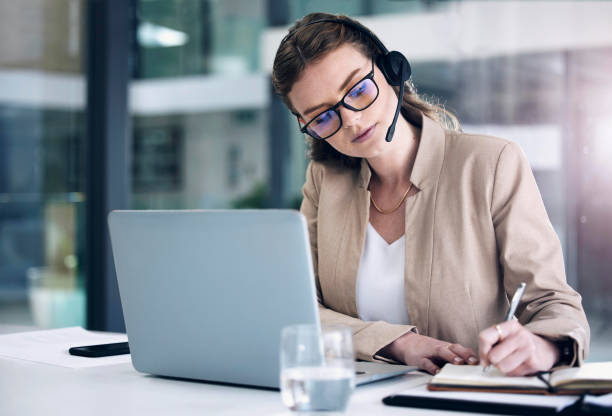 istock Shot of a young call centre agent writing notes while working on a laptop in an office 1372618570