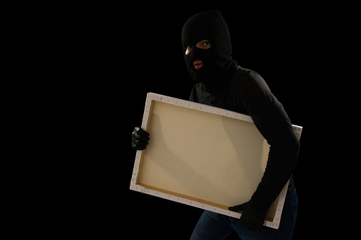 Young thief escaping quietly after a robbery and stealing an art painting while looking at the camera