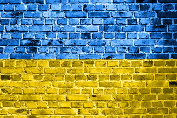 National flag of Ukraine painted on a brick wall. Banner on old brick wall background in cracks blue and yellow colors. The concept of relations between countries - no war between Ukraine and Russia