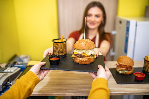 Waitress serving tasty burgers on counter top in fast food restaurant