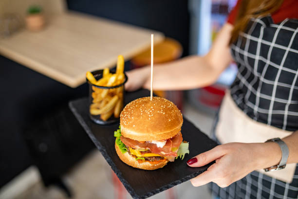 kellnerin trägt einen hamburger mit pommes frites im fast-food-restaurant - sandwich plate food french fries stock-fotos und bilder