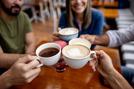 Close-up on a group of friends toasting with cups of coffee at a cafe - food and drink establishment concepts