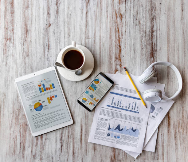 Close-up on a cup of coffee on the table at a cafe with business documents around it. **DESIGN ON SCREEN AND DOCUMENTS WERE MADE FROM SCRATCH BY US**