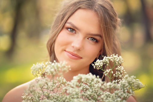 Magnificent young woman surrounded by blossoming flower trees. Gentle makeup, rose lipstick and freely lying long hair curls. Spring style. Symbol of blooming youth.