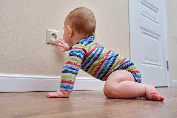 Baby toddler reaches into the electrical outlet on the home wall with his hand. Danger and protection of child fingers from electric shock Baby toddler reaches into the electrical outlet on the home wall with his hand. Danger and protection of child fingers from electric shock emotion regulation in babies stock pictures, royalty-free photos & images