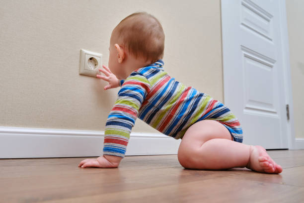 Baby toddler reaches into the electrical outlet on the home wall with his hand. Danger and protection of child fingers from electric shock Baby toddler reaches into the electrical outlet on the home wall with his hand. Danger and protection of child fingers from electric shock babyproof stock pictures, royalty-free photos & images