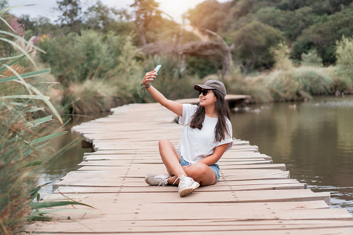 latin young woman taking selfies with smartphone and smiling on a wooden bridge