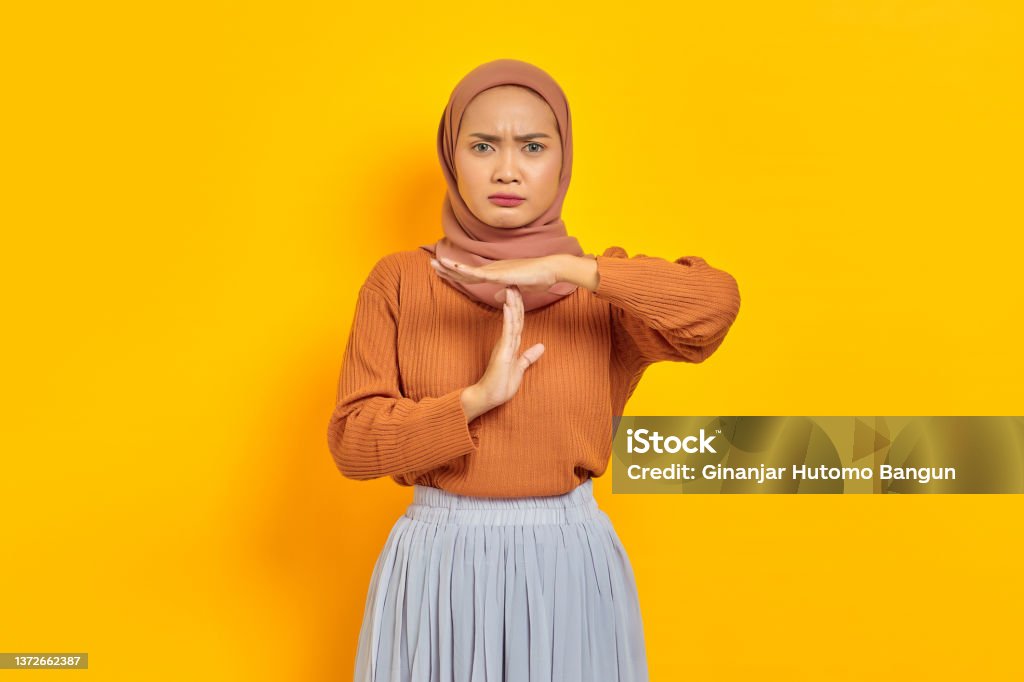 Beautiful young Asian woman in brown sweater and hijab showing time out gesture with hands isolated over yellow background. People islam religious concept 25-29 Years Stock Photo