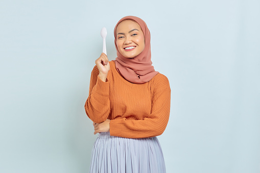 Beautiful young Asian muslim woman in brown sweater licking lips want a delicious meal isolated on white background