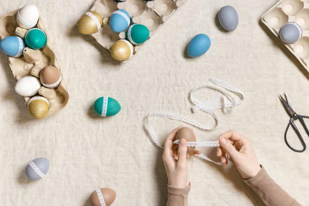 istock Decoration Easter eggs, female hands decorating colorful chicken egg with white tape lace, traditional celebration food and holiday symbol.  Home preparing for Happy Easter. Top view 1372676495