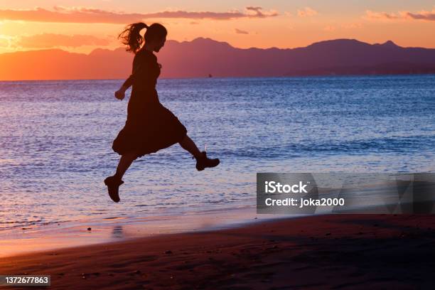 美しい若い女性はサンセットビーチでジャンプ