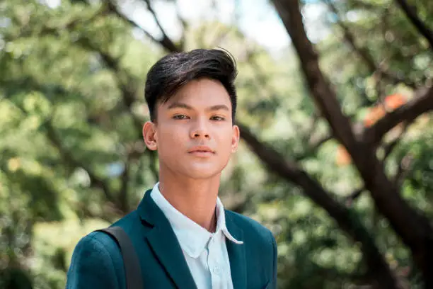 Photo of A handsome and young Filipino college student in smart casual wear. Serious look. At the park or campus grounds.