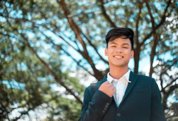 Photo of A handsome and young Filipino college student in smart casual wear. Smiling and friendly vibe. At the park or campus grounds.