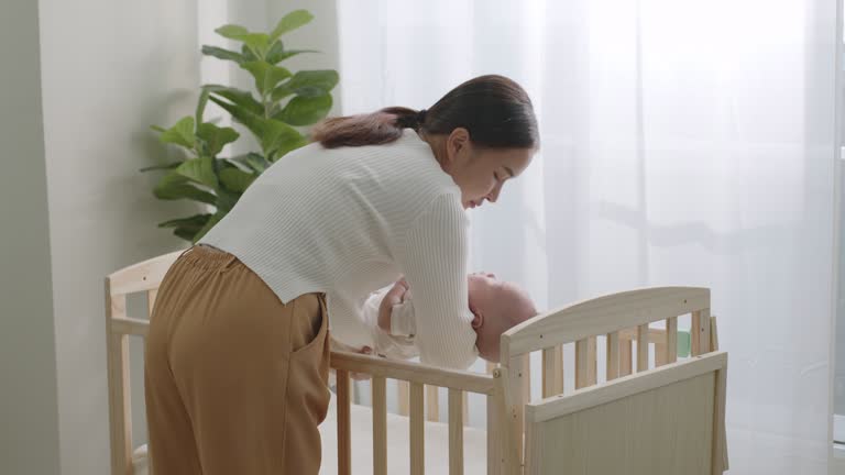 Young Asian Mother put her sleep newborn baby on baby crib.