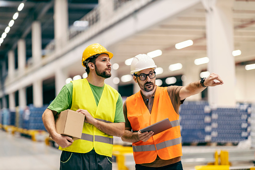 A boss with tablet showing to warehouse worker with box where to put it.