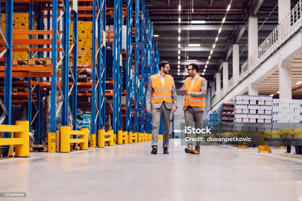 Storage owner with tablet in hands showing around storage to his partner. Warehouse owner touring business partner through the warehouse with tablet in hands. Warehouse Stock Photo