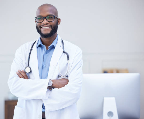 shot of a young male doctor standing with his arms crossed in an office at a hospital - male african descent africa ethnic imagens e fotografias de stock