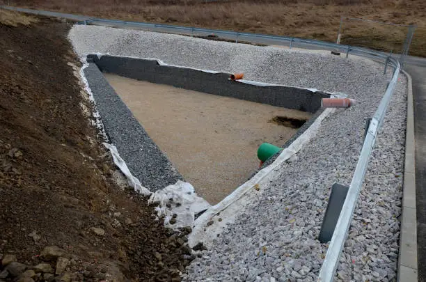 triangle-shaped drainage pond with stone wall paneling and gabion walls. the water slows down during the rain and then overflows from the sewer pipe into the sewer. newly completed waterworks, brakewater, dike, geotextile, stormwater, shatter, lapol