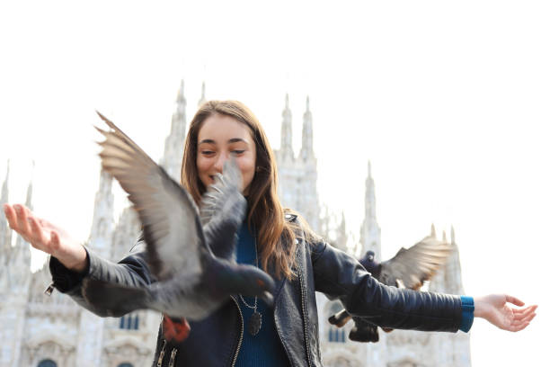 Woman sitting on her bicycle and playing with pigeons at Piazza Duomo in Milan, Italy