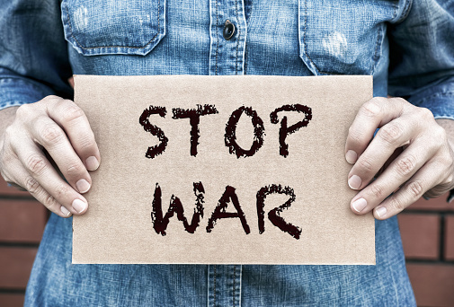 Woman hands holding piece of cardboard with words Stop War against brick wall background.