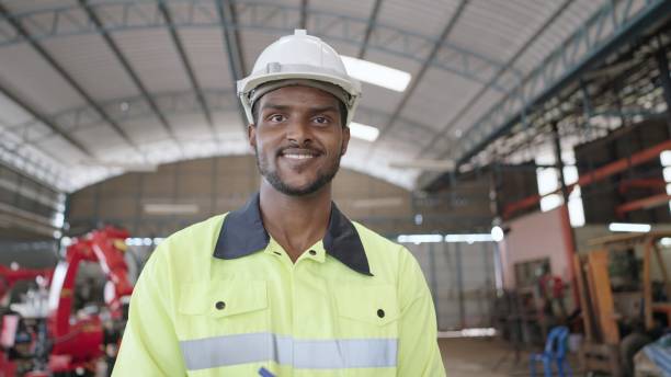istock Professional mechanical male engineer or technician or machinery operator, wearing hard hat,safety uniform, working on production line that uses robots arm to assemble parts. Smiling,looking at camera. 1372708090