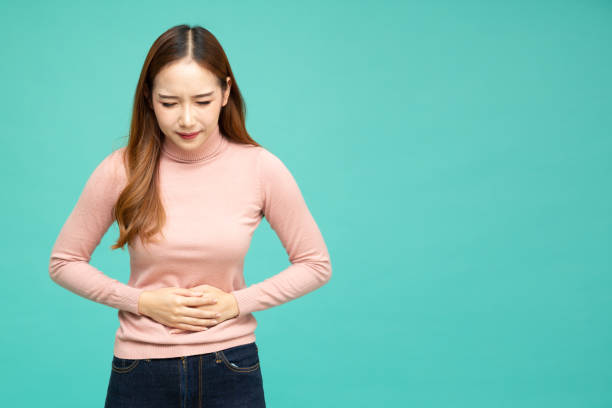 asian woman holding on to her stomach isolated on green background, pain and colic during menstruation - colic imagens e fotografias de stock