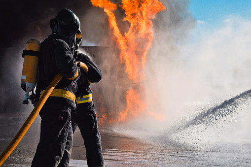 Barcelona, Cataluña, Spain - January 24, 2022: Firefighters and a fire.  They are usiung heavy respiratory protection and wear protective equipment that protects them from the heat and flames.