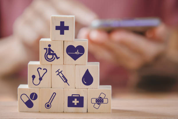 health and medical icon on stack of wooden coins and blurred people holding smartphone for health insurance, wellness, wellbeing concept stock photo