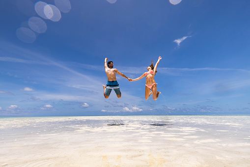 Happy couple having fun while holding hands and jumping high up during summer day on the beach. Copy space.