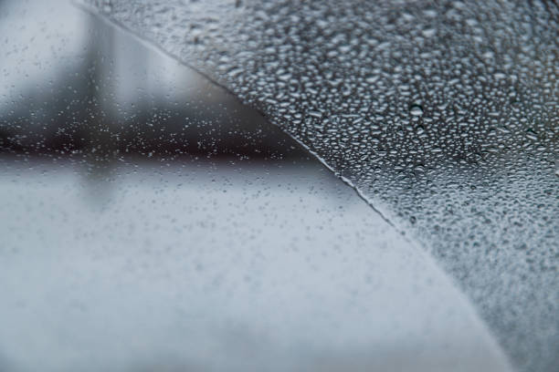 wet windshield vehicle glass covered with water drops partially wiped, blurry overcast weather in the background