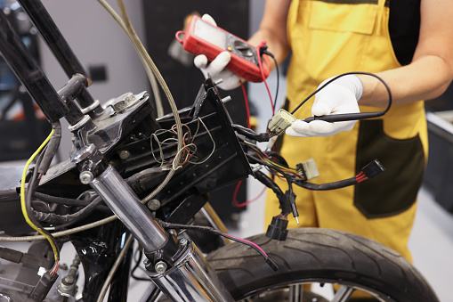 Mechanic using multimeter checks voltage level on motorcycle battery in motorcycle garage. Maintenance and repair concept