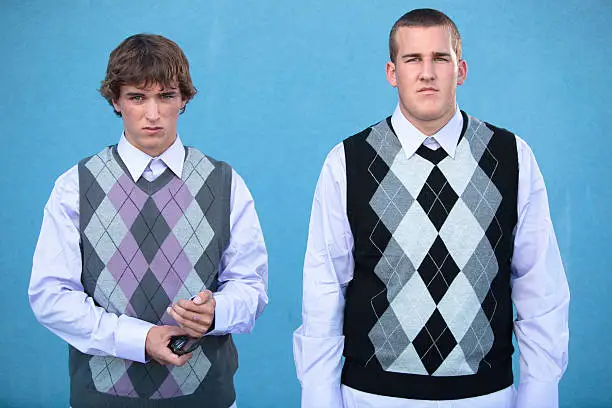 Two geeks standing in sweater vests with serious expressions.