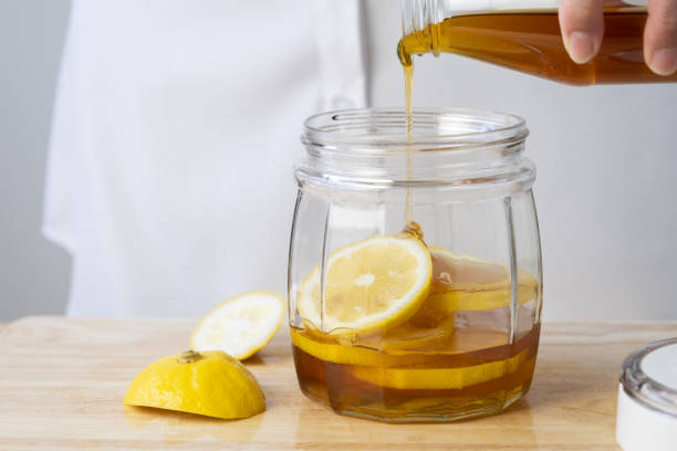istock woman's hand pouring honey in a clear jar with lemon 1372719370