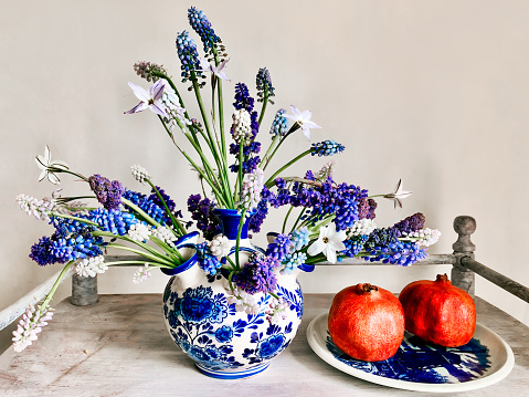 The art of arranging bouquets of flowers. Romantic bouquet in a decorative vase on a coffee table with pomegranate fruits. In composition - muscari and other primroses
