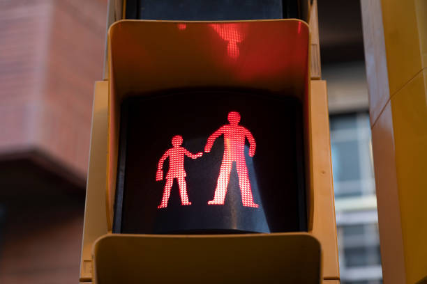 A red traffic light, indicating stop, caution, at a crosswalk in a school zone, shows a figurine of a child and an adult holding hands