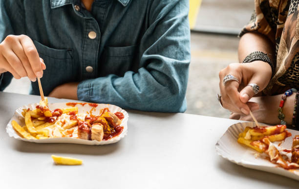 zwei weibliche hände essen currywurst mit pommes frites - currywurst stock-fotos und bilder