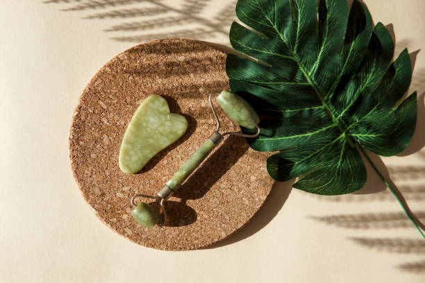 istock Jade Gua sha scraper and face roller massager on a cork round stand with a monstera leaf 1372731242