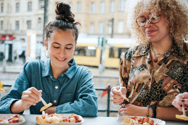 zwei teenager-mädchen essen currywurst mit pommes frites in berlin - currywurst stock-fotos und bilder