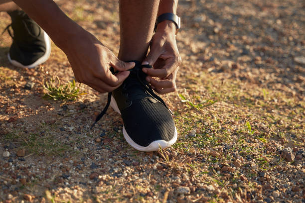 primo piano di un giovane atleta maschio adulto nero che lega i lacci delle scarpe sulla sua scarpa sportiva nera - ewan foto e immagini stock