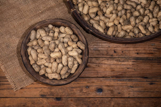 The container on the wood grain table is full of peanuts.
