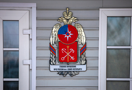 Image of the departmental coat of arms on the administrative building with the inscription in Russian - the Main Directorate of the Ministry of Emergency Situations of Russia in St. Petersburg.