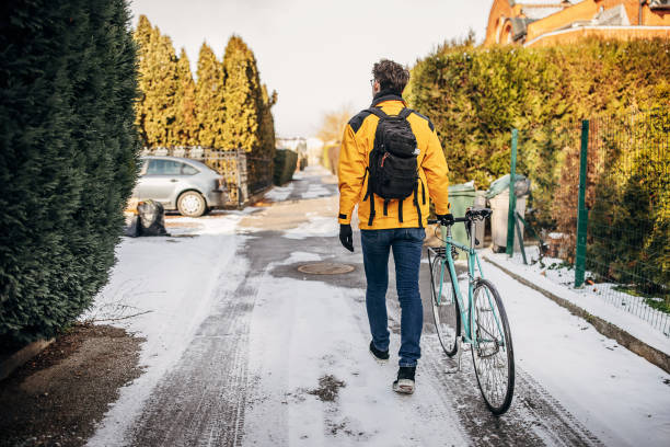 One man, male pushing his bicycle to work on the city street on a winter day.