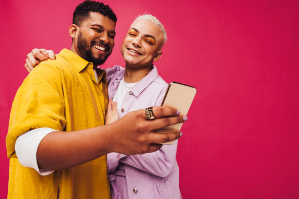 Capturing happy moments in the studio Capturing happy moments in the studio. Cute gay couple smiling cheerfully while taking a selfie using a smartphone. Young gay couple creating memories together in a studio. gay man stock pictures, royalty-free photos & images