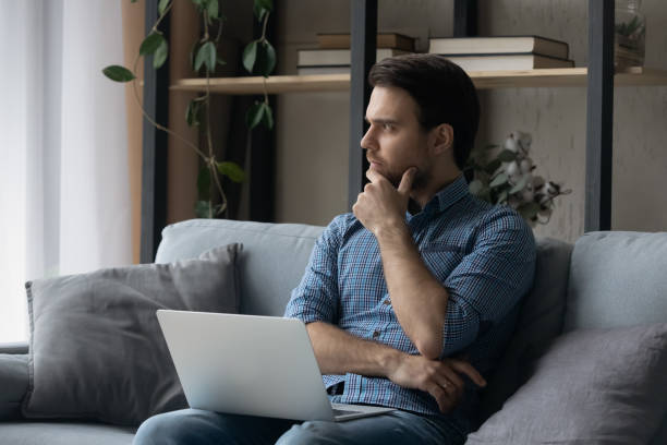 istock Thoughtful man sitting on couch with laptop, looking in distance 1372744098