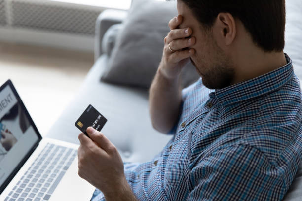 Close up unhappy man having problem with credit card Close up unhappy man having problem with credit card, using laptop at home, depressed frustrated young customer client covering face with hand, loss money, cyber internet fraud and scam concept money cry stock pictures, royalty-free photos & images