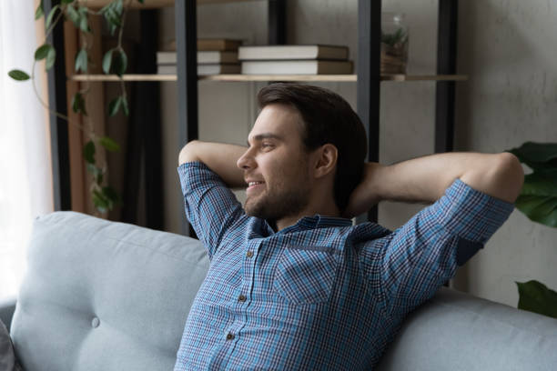 istock Smiling dreamy young man relaxing on couch at home 1372744125
